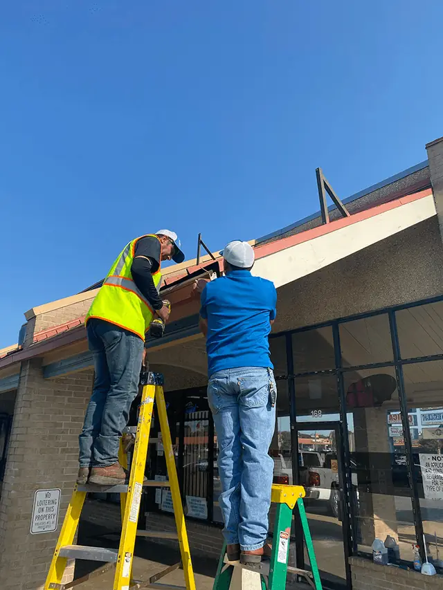 Two CenTex crew on ladders working at a storefront canopy under a clear sky