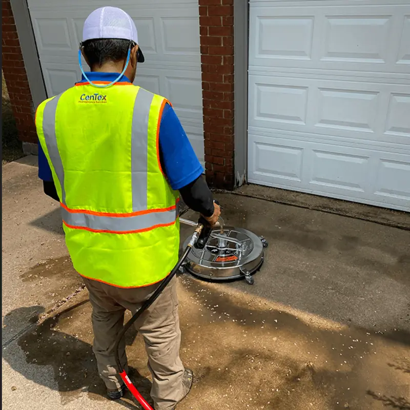 CenTex crew member in a branded hi-vis vest running a surface cleaner across a concrete apron